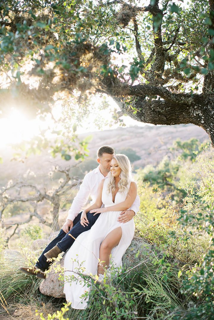 A couple in white clothing sits at Enchanted Rock for engagement photos