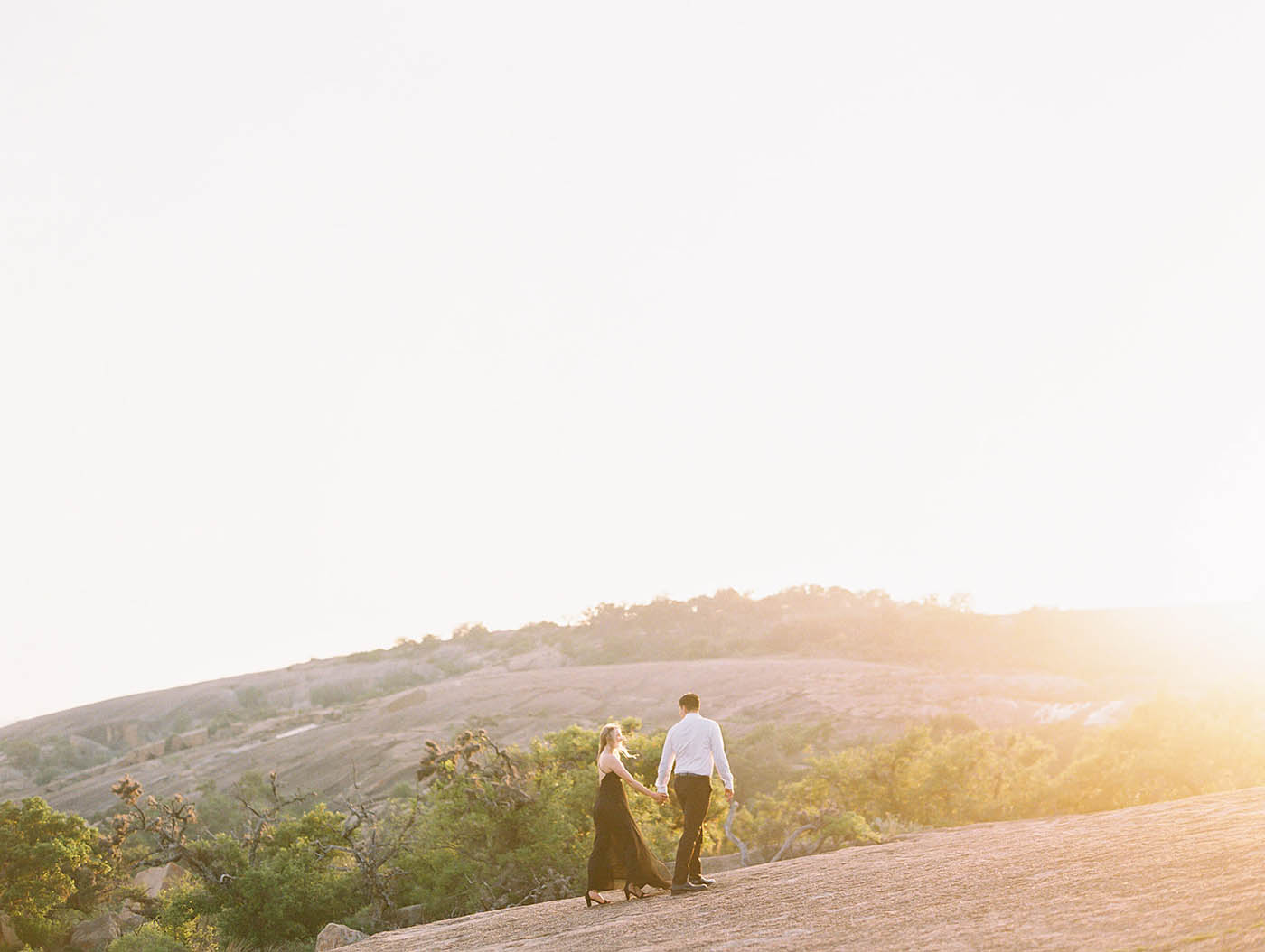 Wide shot of a couple walking across enchanted rock at sunset