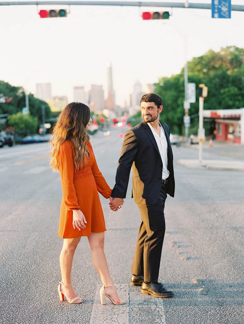 woman in orange dress walks with her fiance across south congress