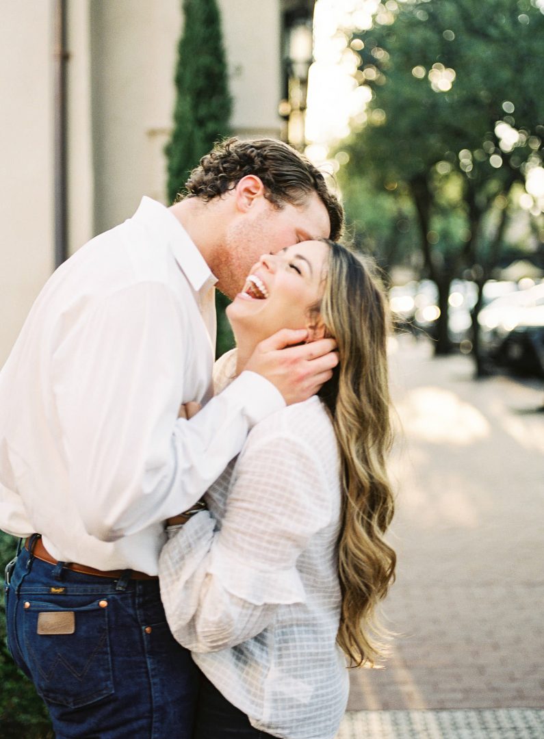 woman in white shirt laughs while her fiance whispers in her ear