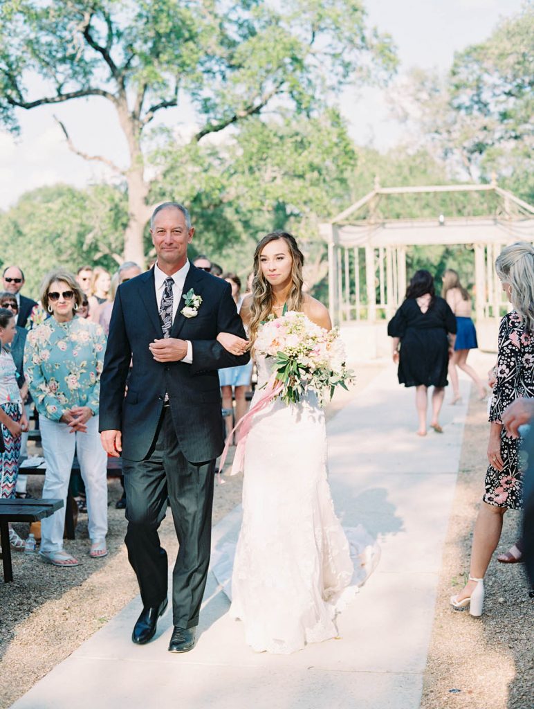 the bride walks down the aisle escorted by her father