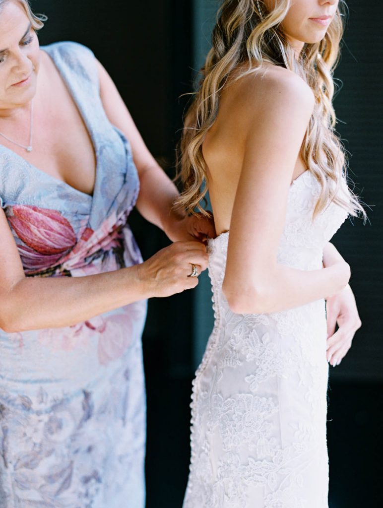 the mother of the bride zips up the bride's dress