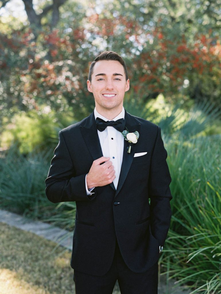 The groom poses for a portrait in a black tuxedo