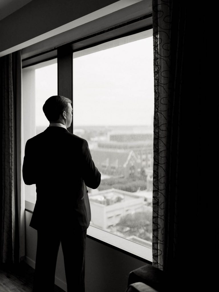 the groom looks out the window of the Worthington Renaissance in Fort Worth