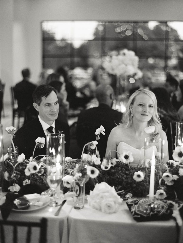 bride and groom smile at their guests while seated for dinner