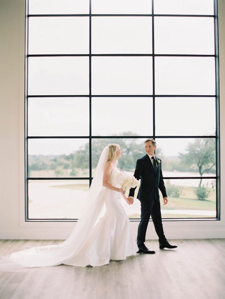 bride and groom walk in front of a large window