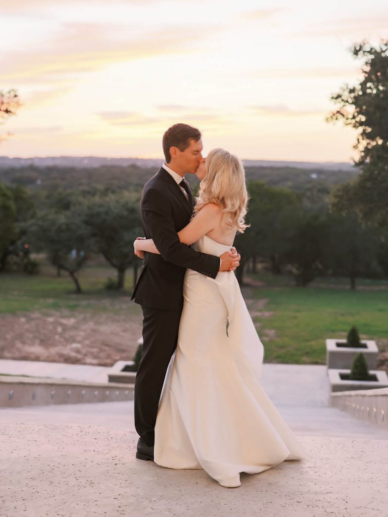 bride and groom kiss in front of a sunset
