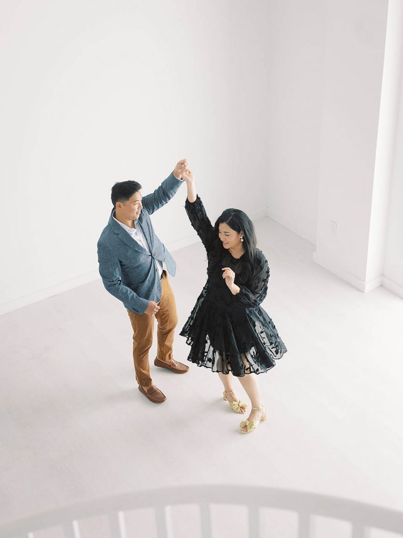 woman in black dress and man in blue jacket twirl for engagement photos at the Lumen Room in Austin, Texas