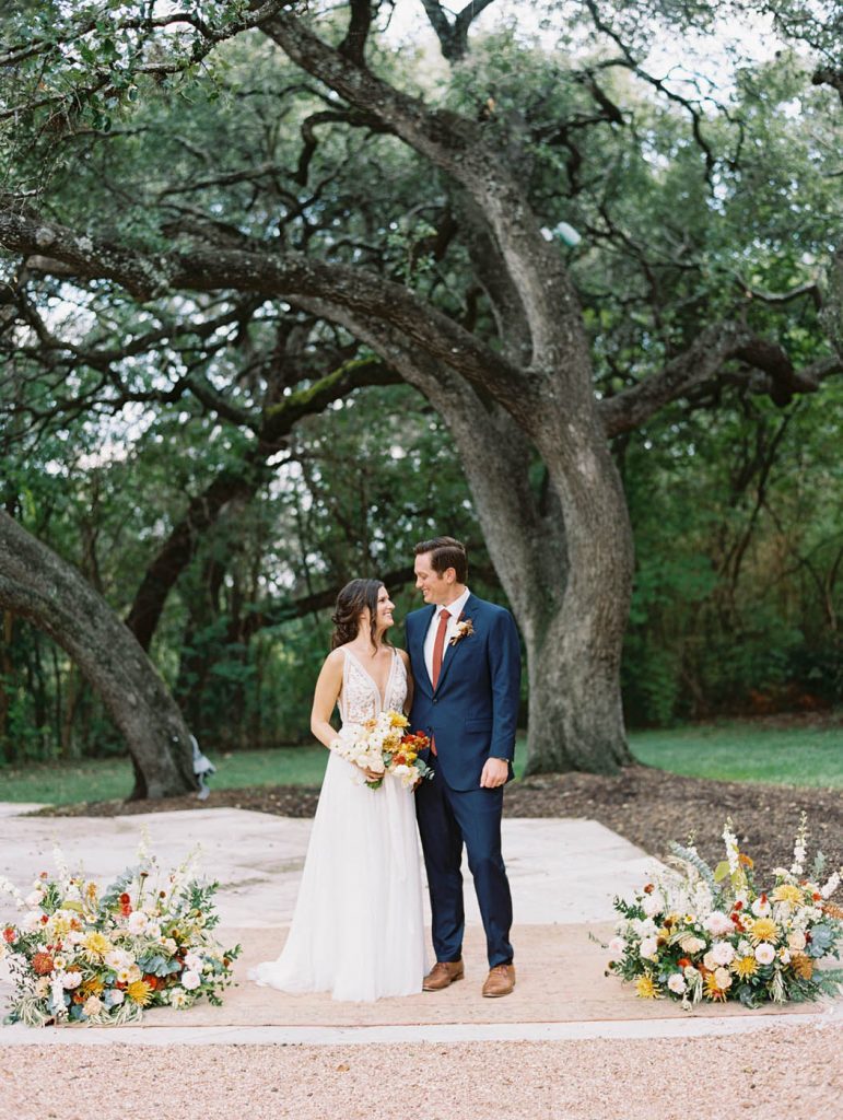 a bride and groom posing together in front of flowers under an oak tree