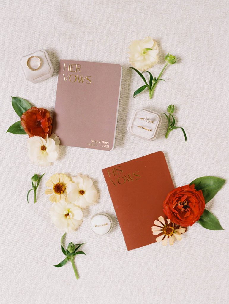 a flatlay with wedding vowbooks, flowers, and rings