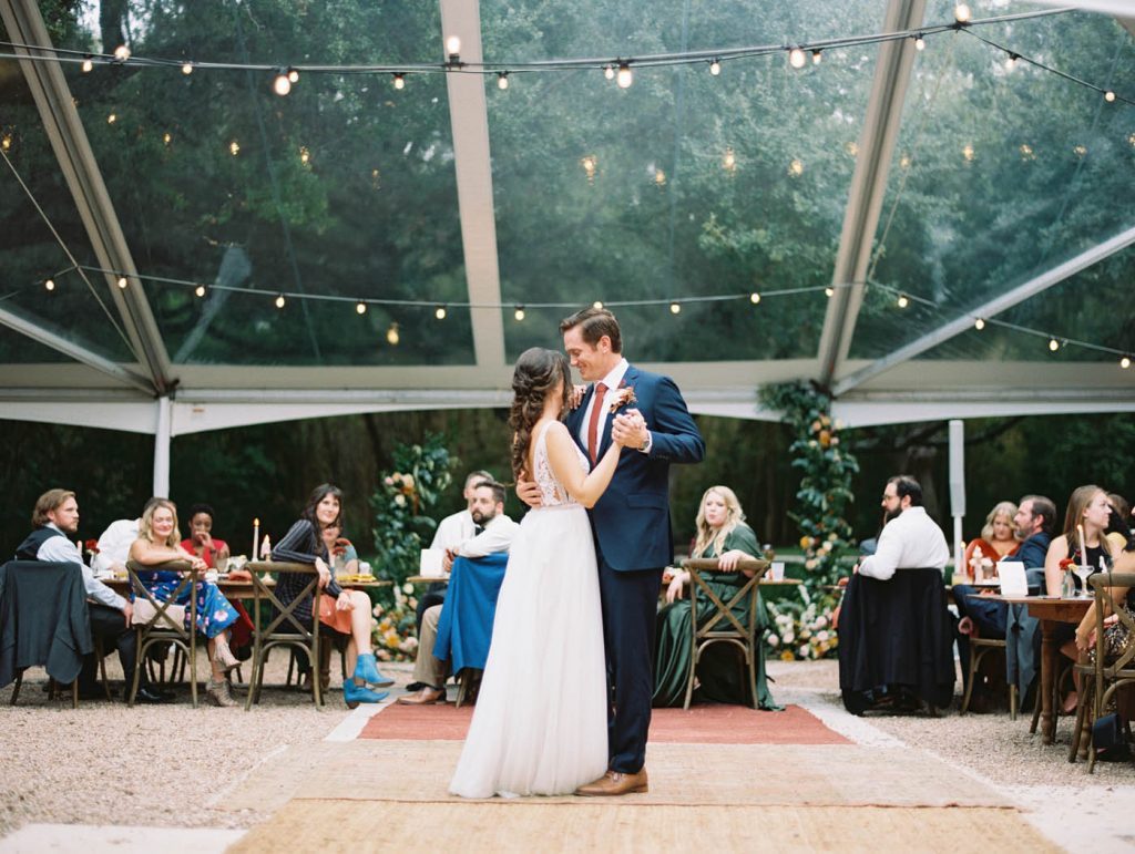 the bride and groom have their first dance under a clear tent