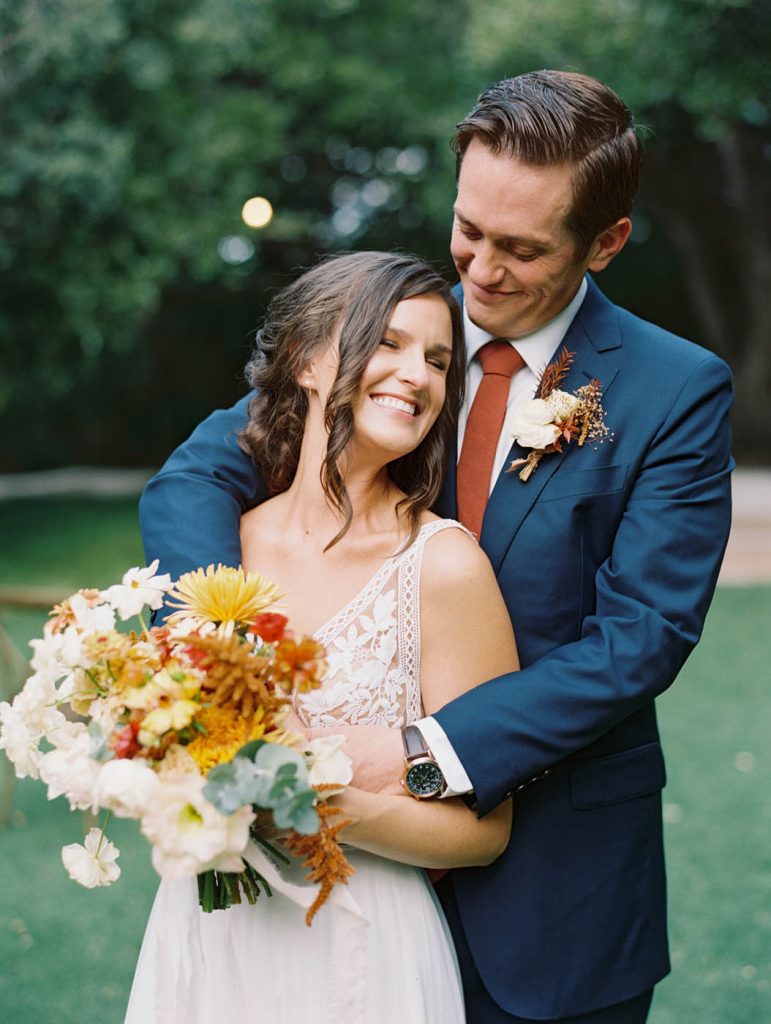 the bride and groom embracing and laughing with an autumnal wedding bouquet