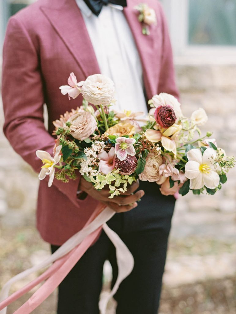 groom in pink jacket holding a pink wedding bouquet
