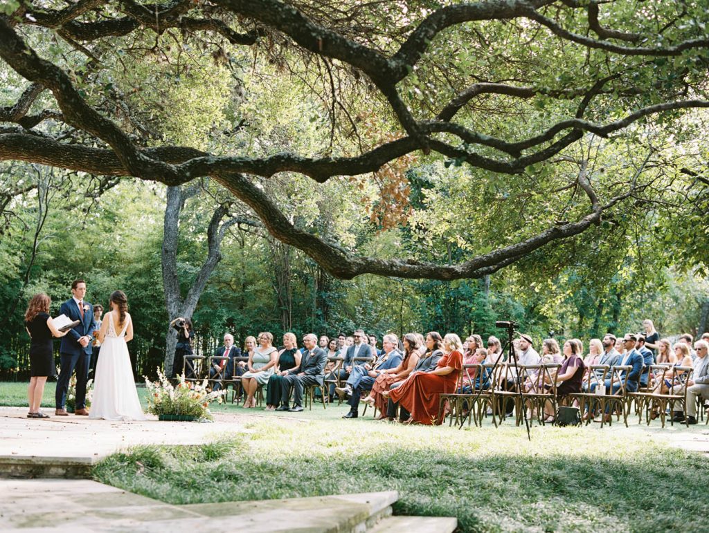 a wide photo from the side of the wedding ceremony under an oak tree at mercury hall