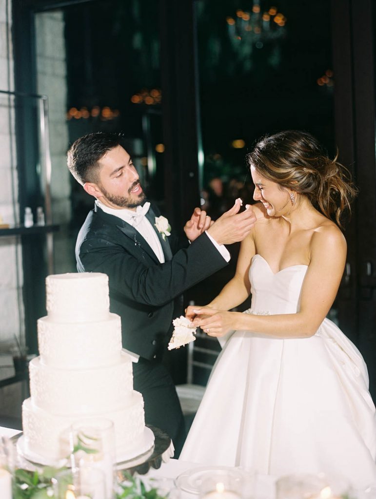 groom playfully puts cake frosting on the bride's nose