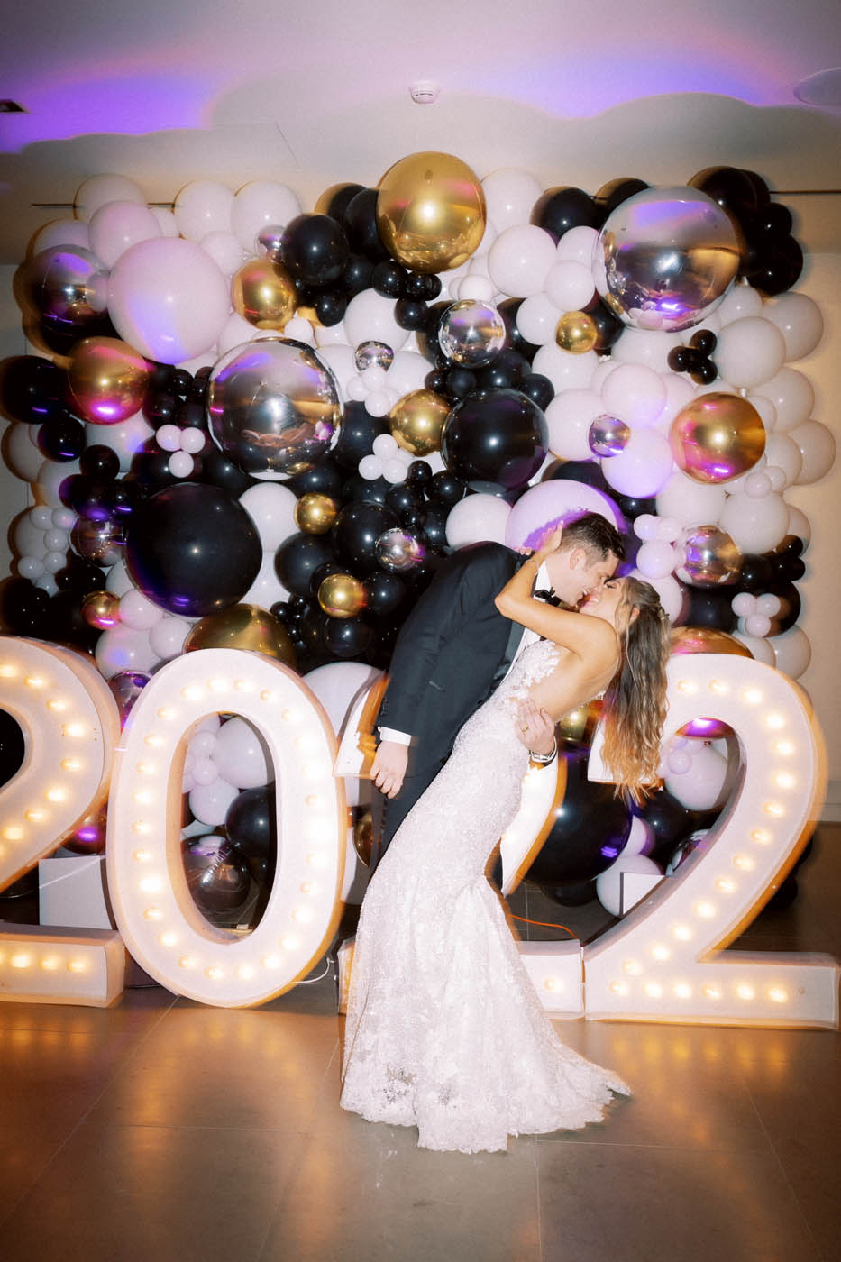 the bride and groom kiss in front of a balloon wall that says 2022