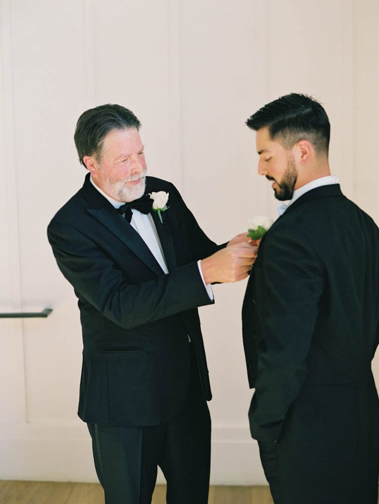 the father of the groom helping his son with his boutonniere