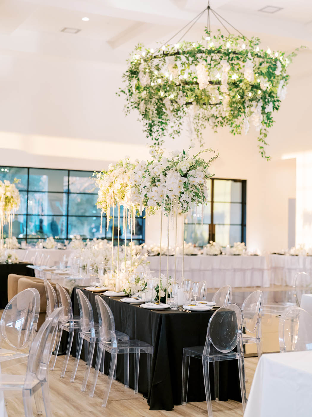 A black reception table with ghost chairs and white and green florals
