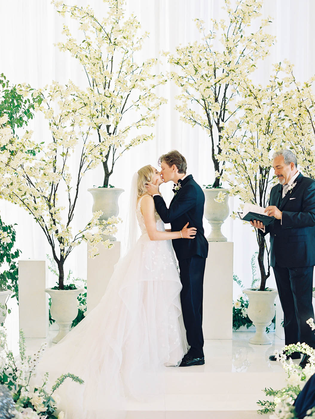 the bride and groom kiss at their ceremony with indoor trees