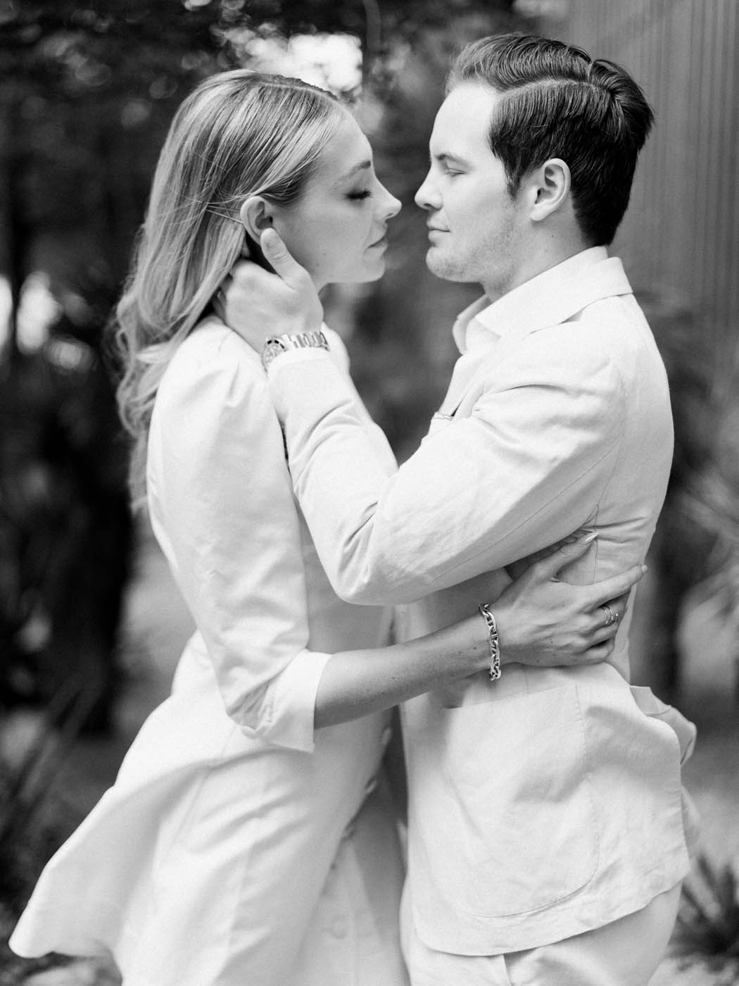 a bride in a short white dress and groom in a khaki suit pull each other in for a kiss