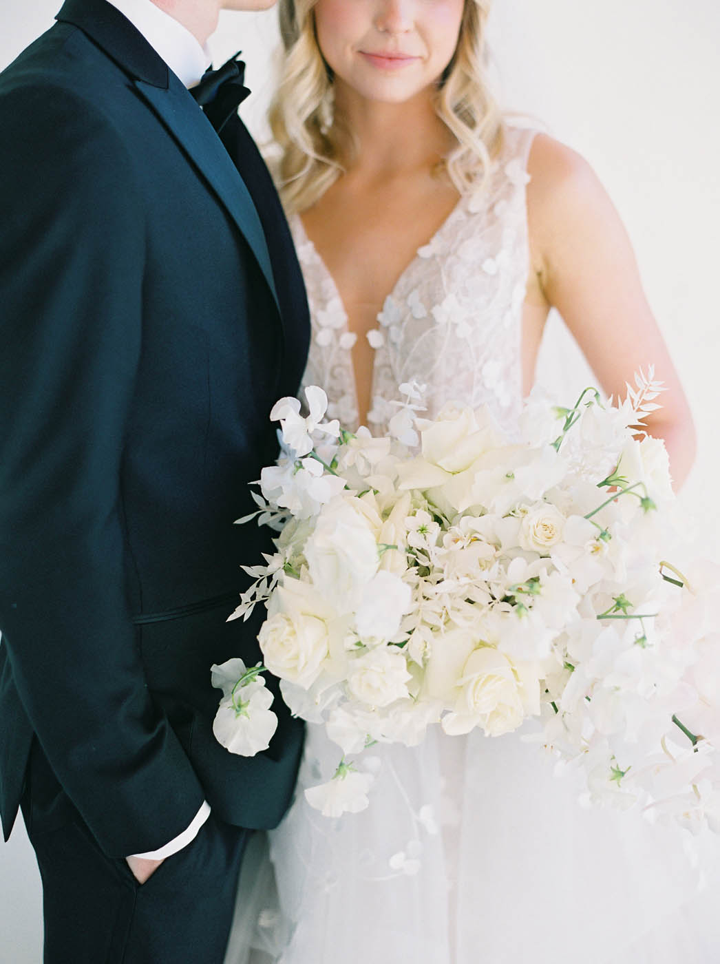 the bride holds her tonal white modern bouquet against the groom's black tux