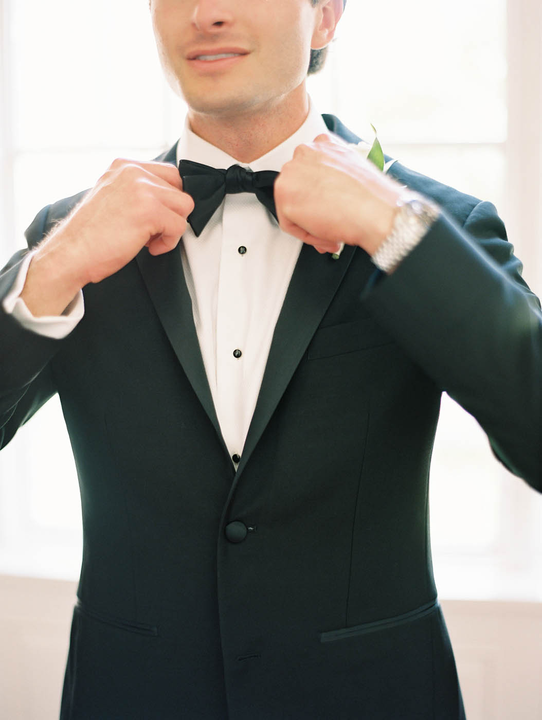 An up close shot of the groom tying his bow tie