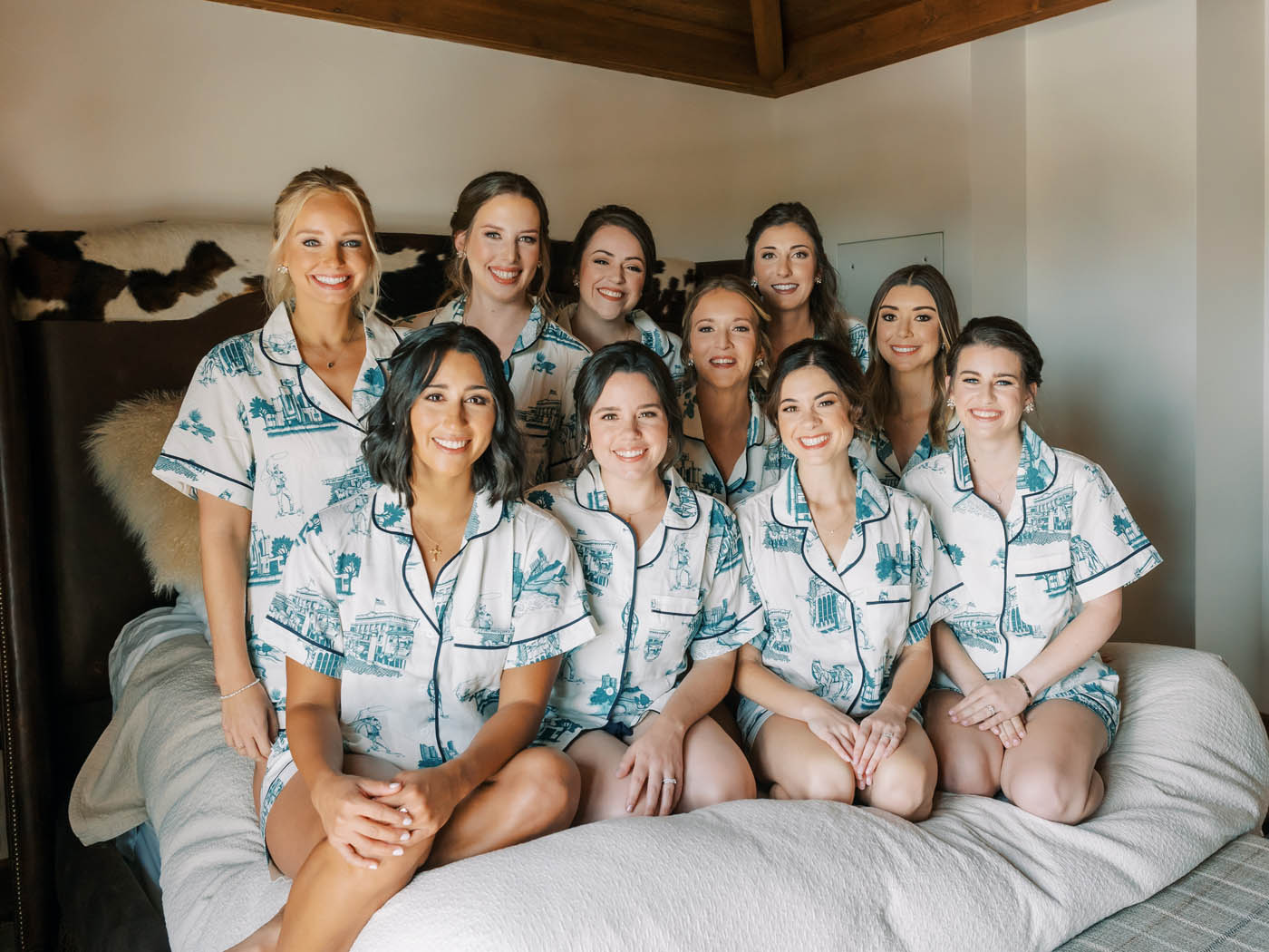 Bridesmaids in custom pajamas pile on the bed at Hotel Drover